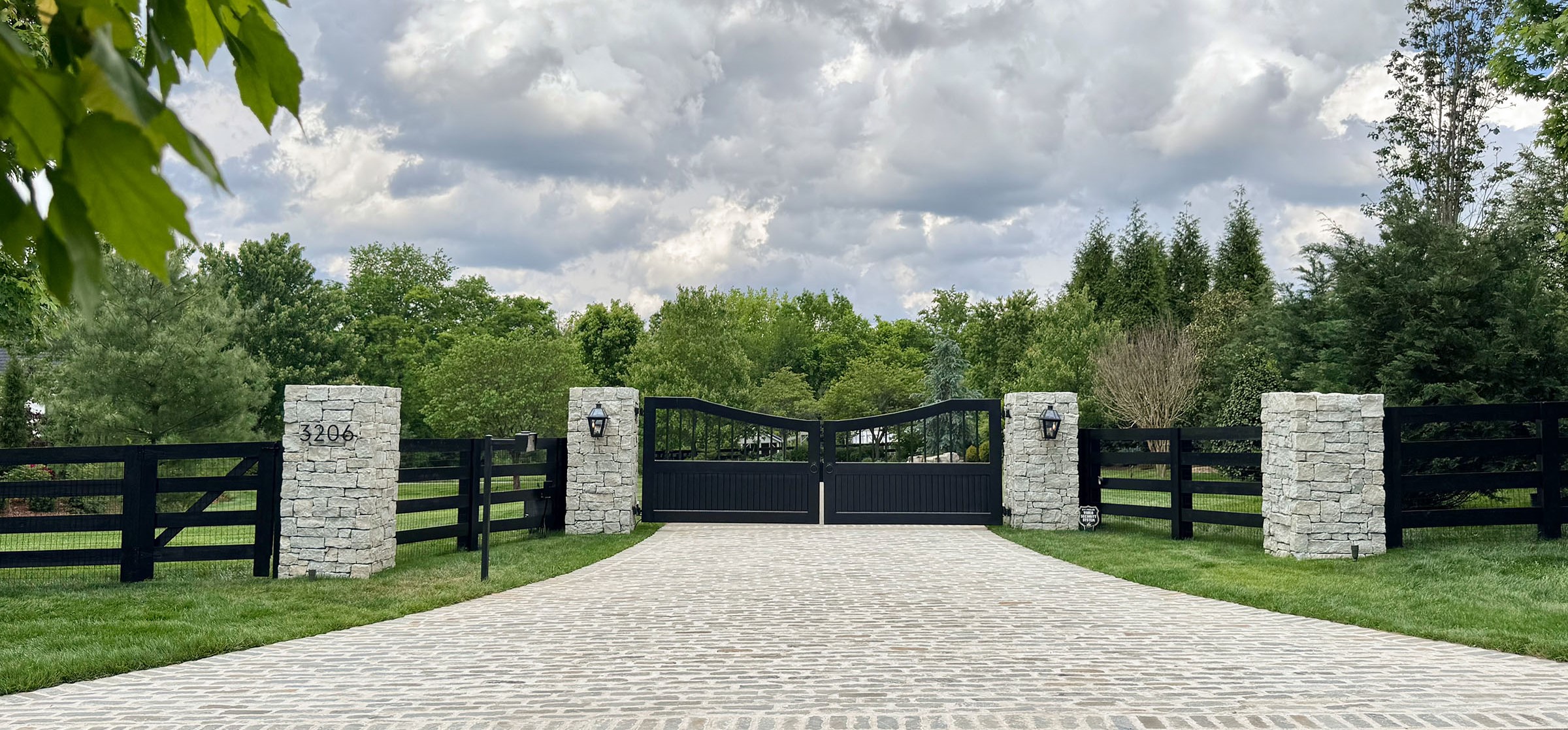 Large black swing gate with stone columns on a cobblestone driveway in Middle Tennessee.