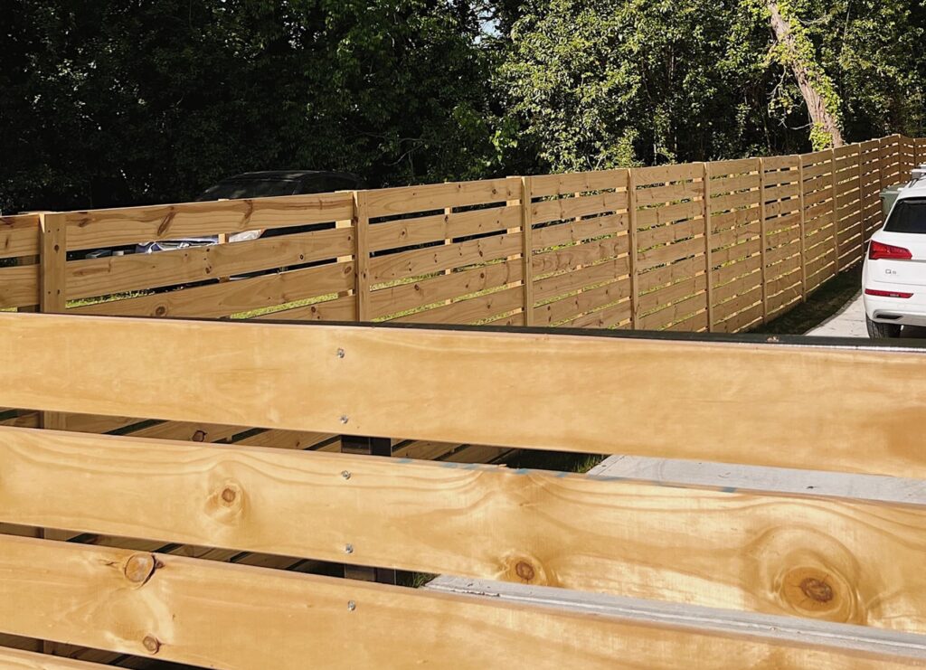 A long horizontal-style wood privacy fence lining a suburban driveway.