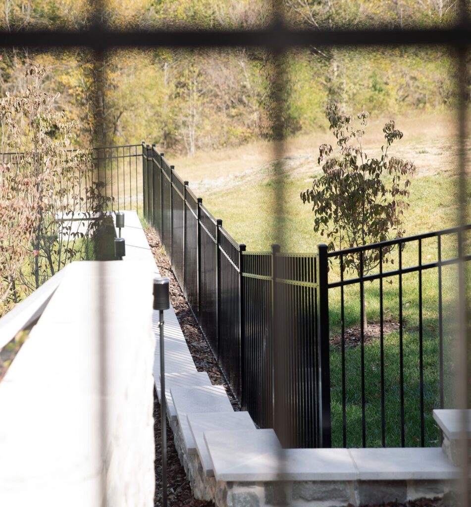 Black aluminum fence along a landscaped yard, viewed through a window.