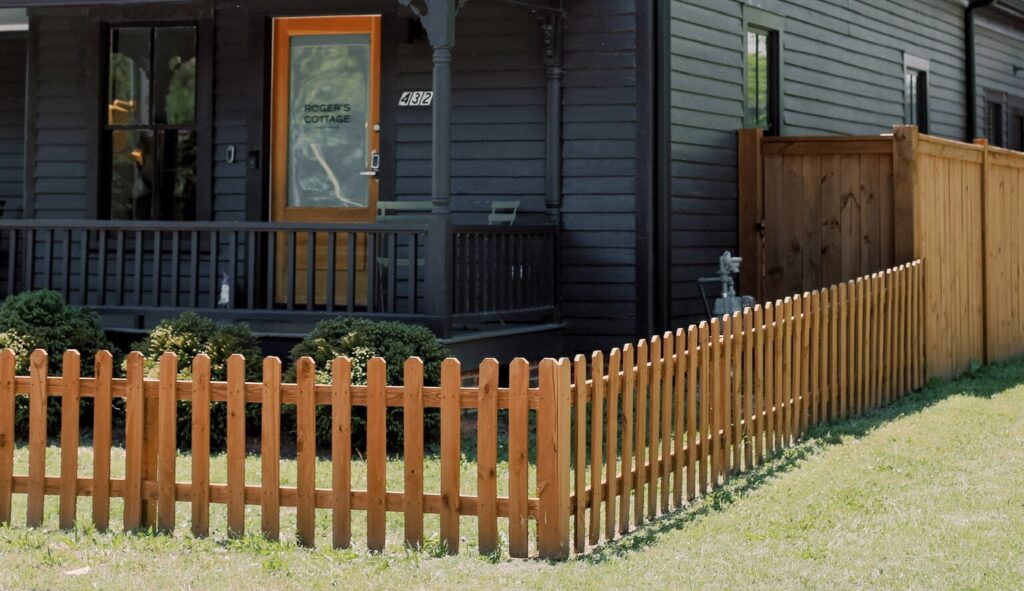 A natural wood picket fence in front of a black cottage in Nashville, paired with a taller privacy fence along the side yard.